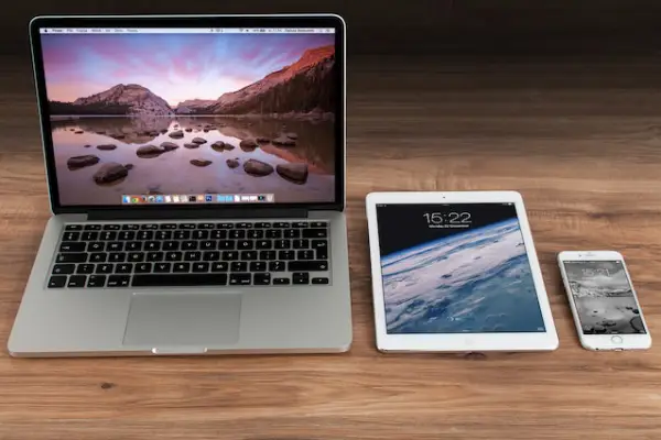 An open MacBook, iPad and iPhone laid down side by side on a wooden floor.