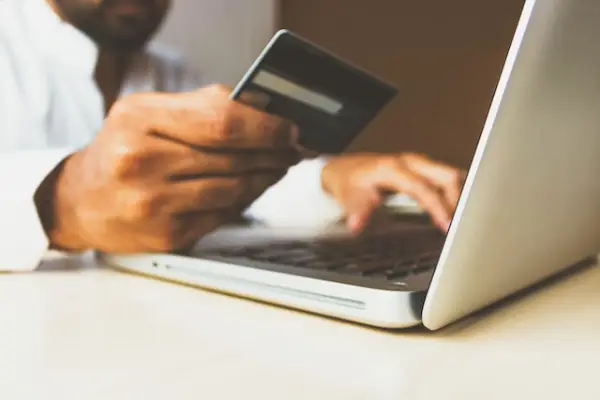 A person looking at a credit card on the right hand and typing on a laptop using the left hand