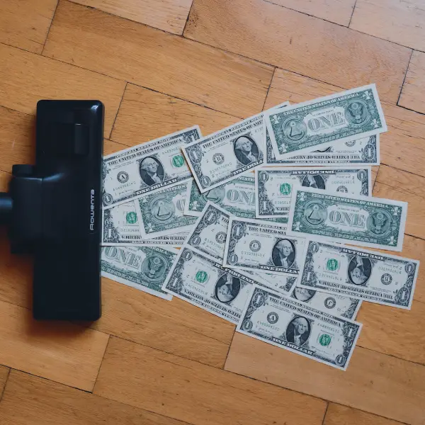 Vacuuming dollar currency notes from a wooden floor