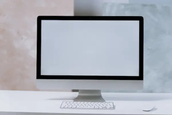 An iMac with white screen, wireless Apple keyboard and mouse on a white table.