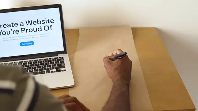 A gif image of a person about to write on a brown paper sheet with an open MacBook beside the paper with the text "Create a Website You're Proud Of."