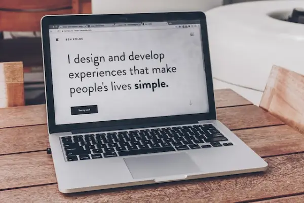 A laptop on a wooden table with a web browser open to a web page with the words "I design and develop experiences that make people's lives simple."