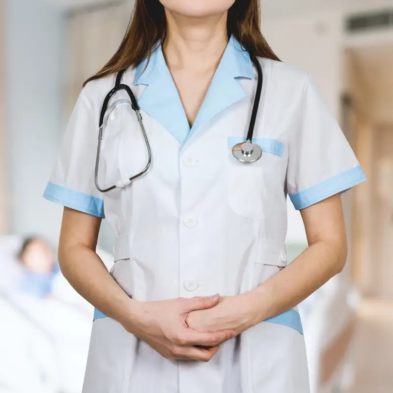 A female nurse standing with her hands held together in front and a stethoscope hanging over her shoulders