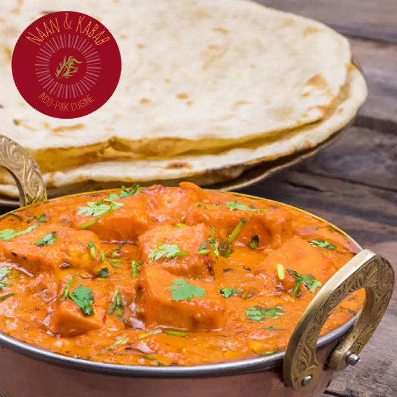 Butter chicken in a traditional Indian bowl in front of a plate of naan breads