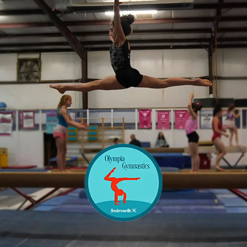 A young girl performing a perfect gymnastic split in the air, inside a gymnasium