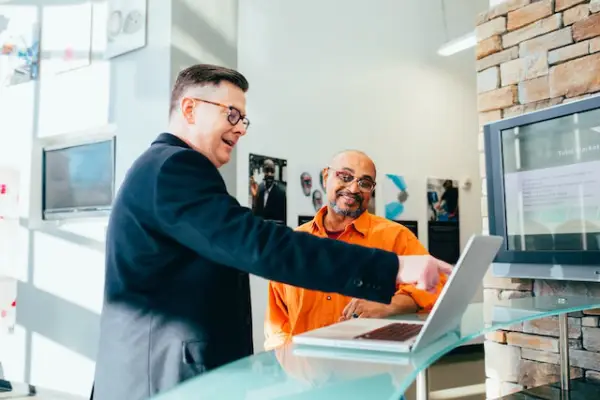 A man pointing at a laptop screen while another man looks on.